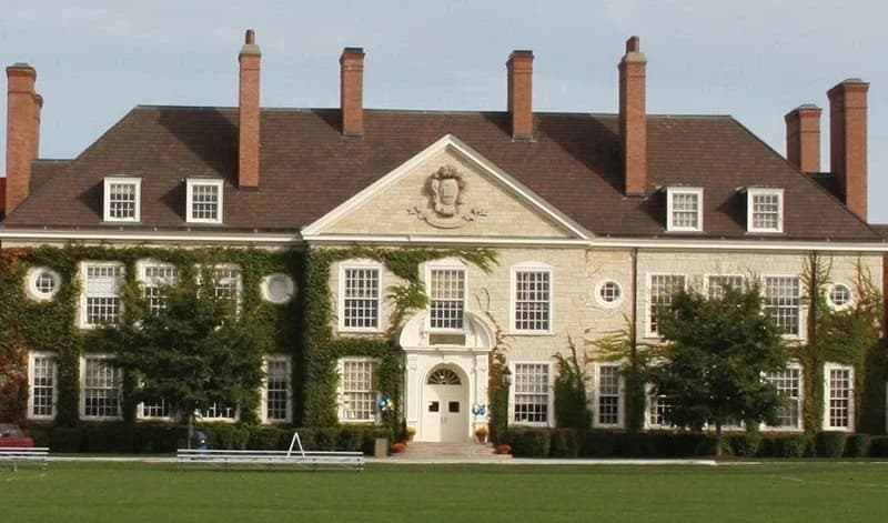 Historic school facade with ivy-covered masonry, tall chimneys, and a broad front lawn