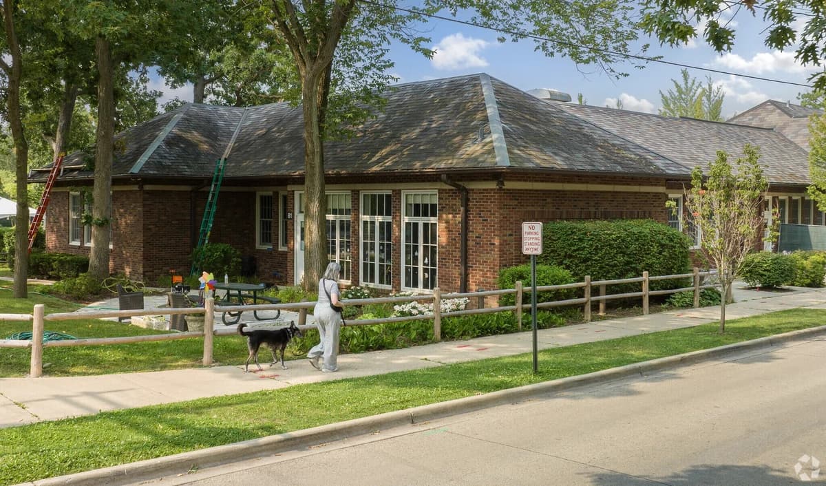 Low brick school building with tall windows, a pitched roof, and a tree-lined sidewalk