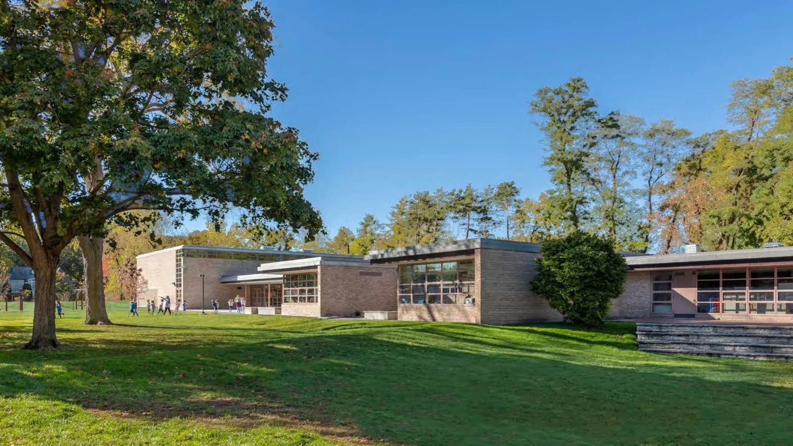 Crow Island Elementary School's low brick addition and large classroom windows opening toward a tree-lined lawn